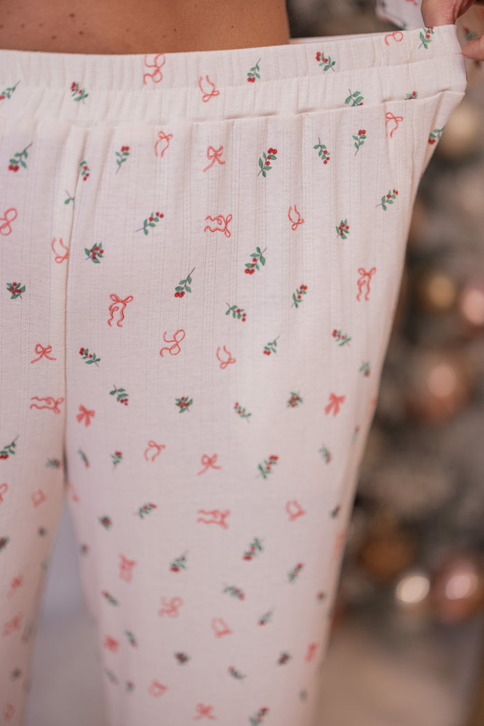 Women's cream pointelle knit pajamas with red, pink and green holly and bow tie print by Peach Love California showing elastic waistband