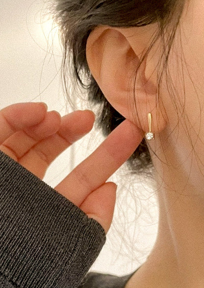 A woman wearing a gold hook earring with a cubic zirconia solitaire gem.