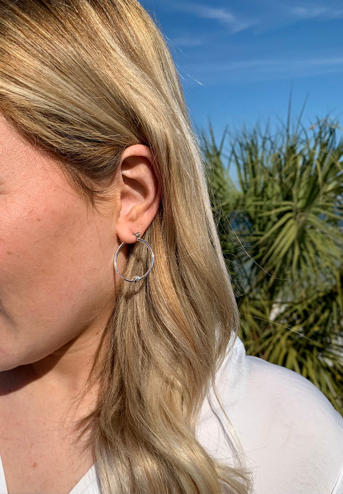 Silver Kelly hoop earrings with a knot detail on the bottom center of the earring in an ear