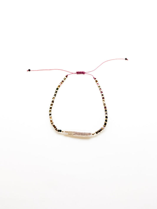 A purple bracelet with a baroque-style pearl and earthy-toned beads, featuring a sliding knot closure.