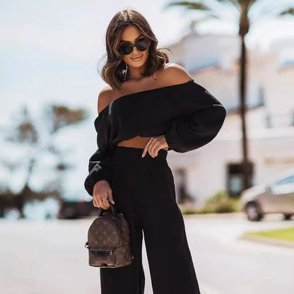 Woman in black off-shoulder top and pants holding a small backpack on a street.