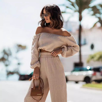 Woman in beige off-shoulder top and pants holding a brown handbag outdoors.