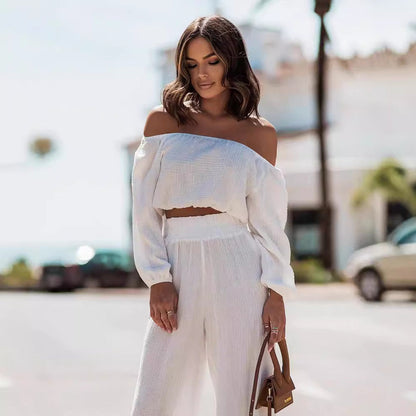 Woman wearing a white off-shoulder top and pants with a blurred street background