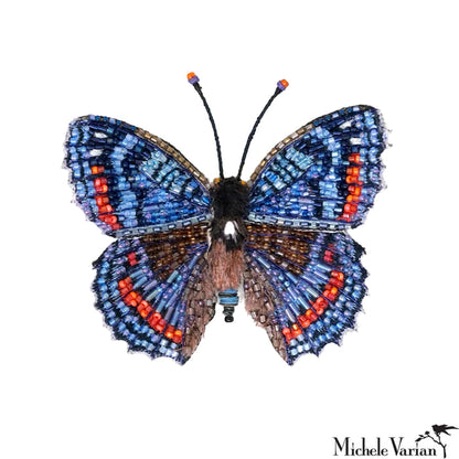 Butterfly-shaped brooch with blue, orange, and brown colors on a white background